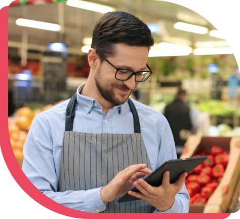 Empleado de supermercado en sección de frutas usando tablet para gestionar tareas operativas con la aplicación Frogm